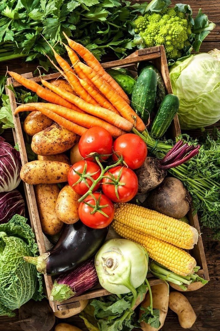 A wooden crate filled with fresh carrots, tomatoes, potatoes, corn, cabbage, eggplant and other seasonal vegetables