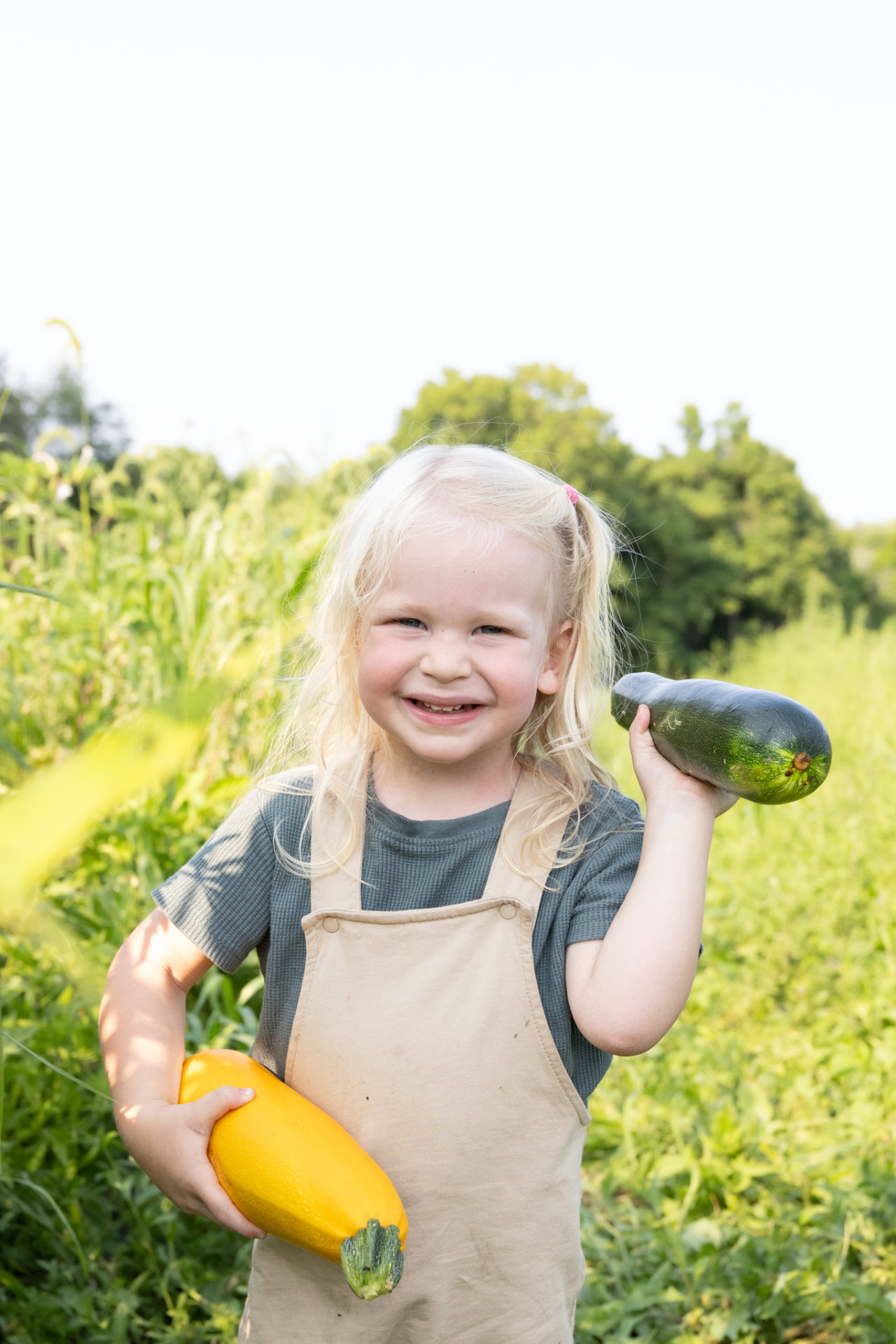 Smiling child holding a yellow squash and zucchini in the garden